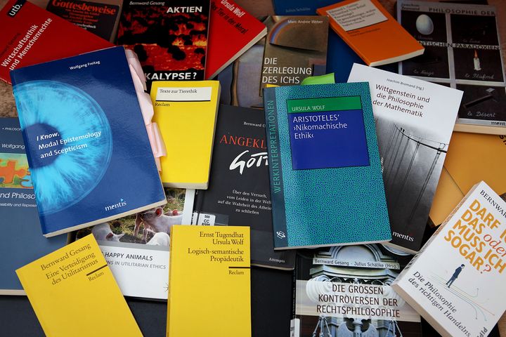 Etwa ein Dutzend verstreute Bücher mit Titeln aus unterschiedlichen Themenbereichen der Philosophie. Erkennbar sind Namen wie "Wittgenstein" oder "Aristoteles" sowie Begriffe wie "Gott", "Ich", "Recht" oder "Aktien". 