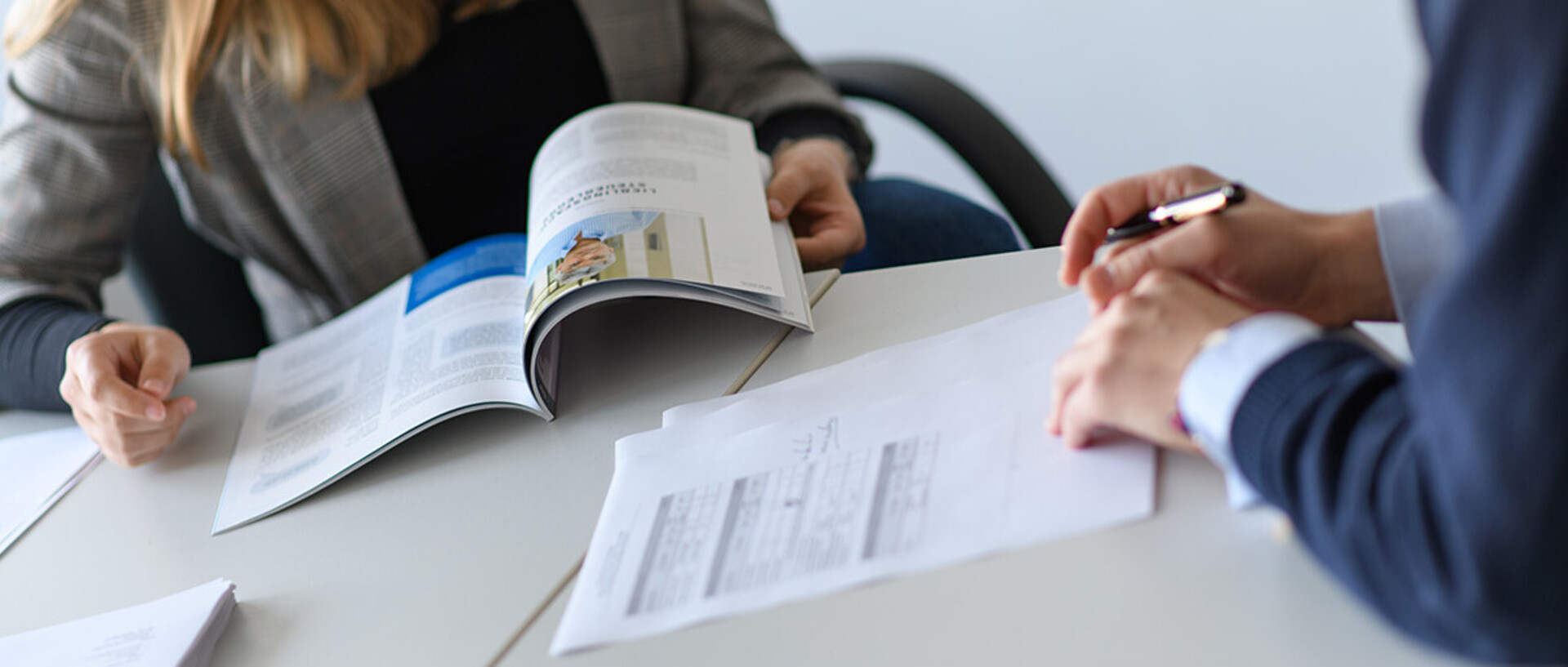 Zwei Menschen blättern in Dokumenten an einem Tisch.